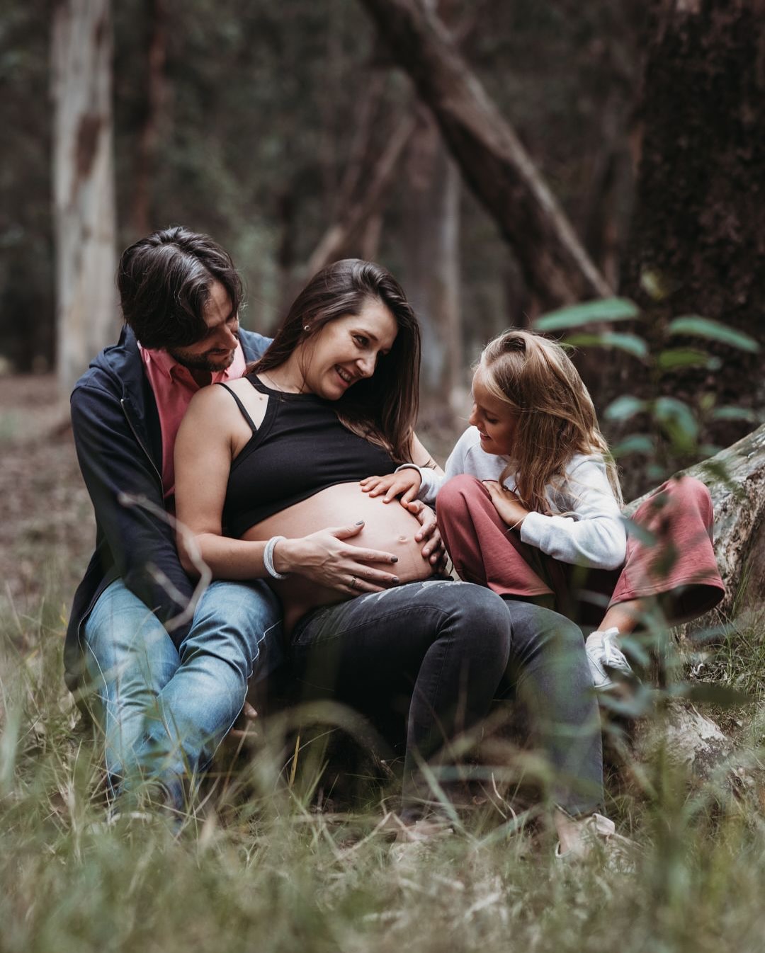 Familia embarazada en el bosque, la hermana mayor acaricia la panza